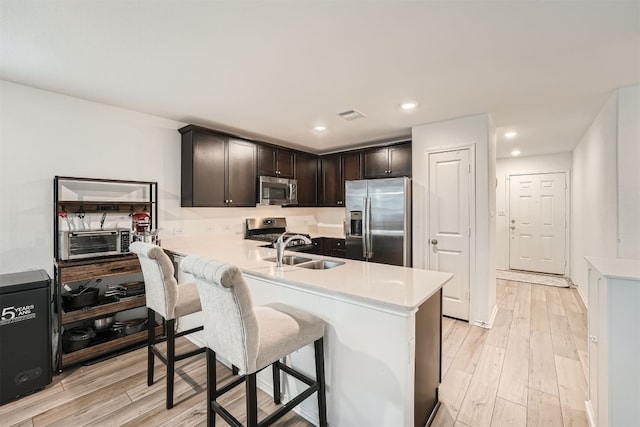 kitchen featuring a kitchen breakfast bar, sink, appliances with stainless steel finishes, light hardwood / wood-style floors, and dark brown cabinetry