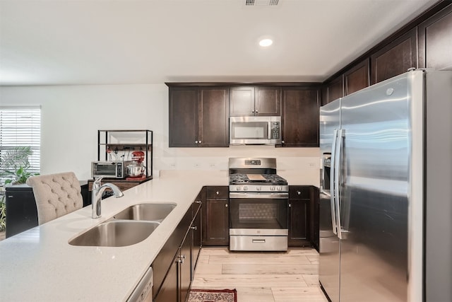 kitchen featuring appliances with stainless steel finishes, light stone counters, dark brown cabinets, sink, and light hardwood / wood-style floors