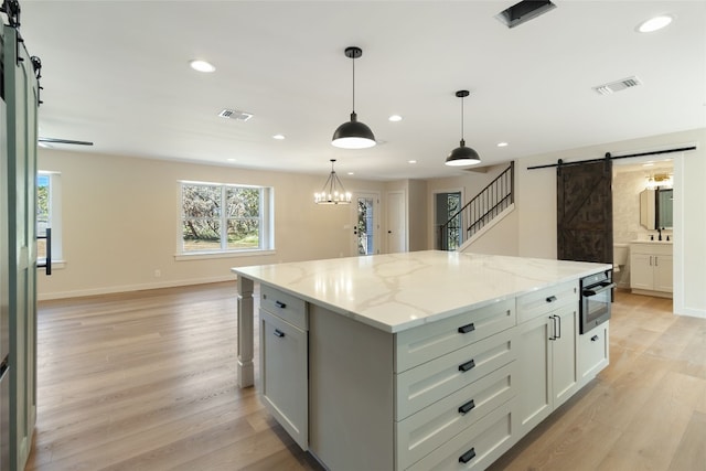 kitchen with light stone countertops, a barn door, a center island, decorative light fixtures, and light hardwood / wood-style flooring