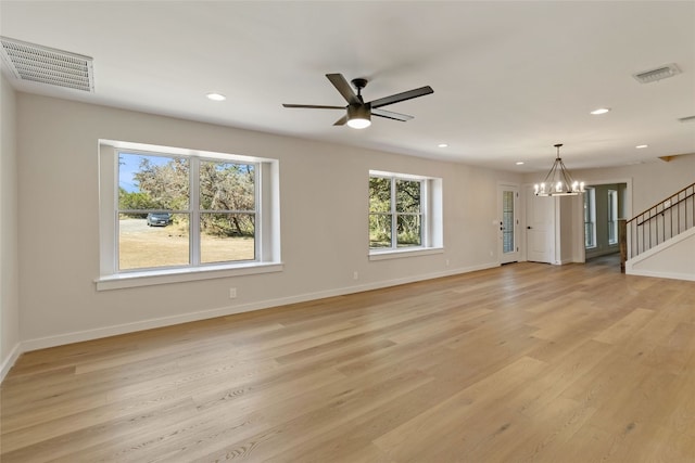 unfurnished living room with light hardwood / wood-style flooring, ceiling fan with notable chandelier, and plenty of natural light