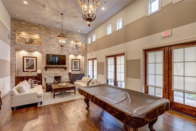 recreation room with hardwood / wood-style floors, billiards, a fireplace, a towering ceiling, and french doors