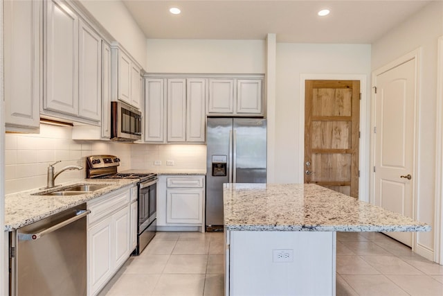 kitchen featuring a kitchen island, stainless steel appliances, sink, light tile patterned floors, and light stone counters