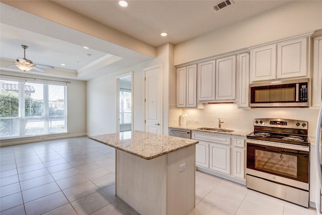 kitchen featuring a kitchen island, stainless steel appliances, sink, light stone countertops, and tasteful backsplash