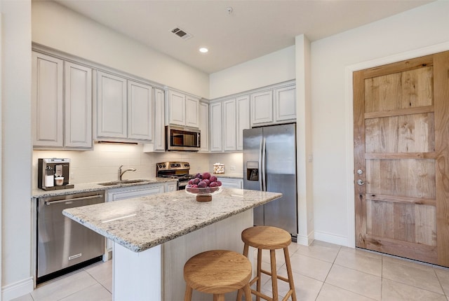 kitchen with a kitchen island, a kitchen breakfast bar, stainless steel appliances, sink, and light stone countertops