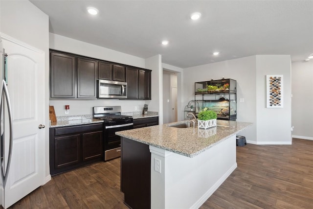 kitchen with a kitchen island with sink, light stone counters, dark hardwood / wood-style flooring, and stainless steel appliances