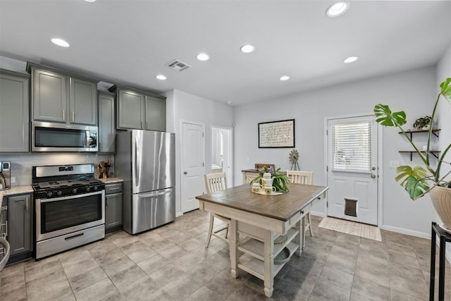 kitchen with tasteful backsplash, gray cabinetry, light stone countertops, and appliances with stainless steel finishes