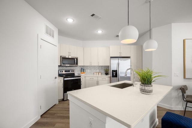 kitchen with appliances with stainless steel finishes, sink, pendant lighting, hardwood / wood-style floors, and white cabinetry