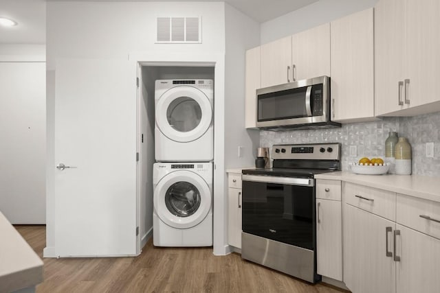 kitchen with stacked washer / dryer, decorative backsplash, stainless steel appliances, and light hardwood / wood-style floors