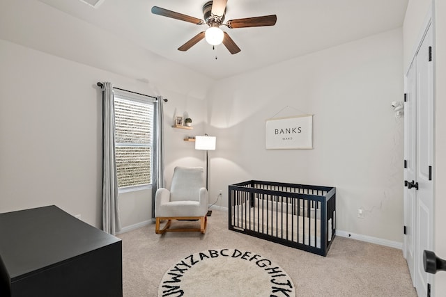 carpeted bedroom with a crib and ceiling fan