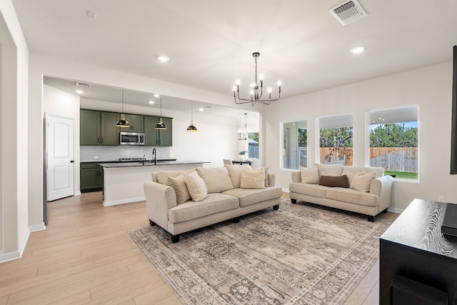 living room with a notable chandelier, sink, and light hardwood / wood-style flooring