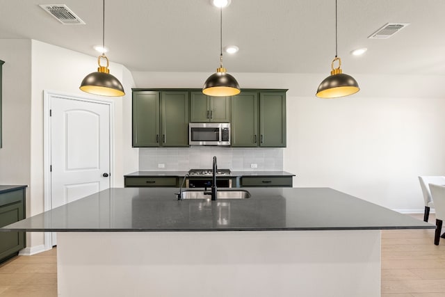 kitchen featuring decorative backsplash, sink, hanging light fixtures, and an island with sink