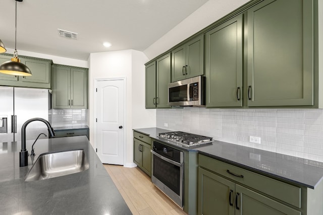 kitchen with appliances with stainless steel finishes, tasteful backsplash, sink, decorative light fixtures, and green cabinets