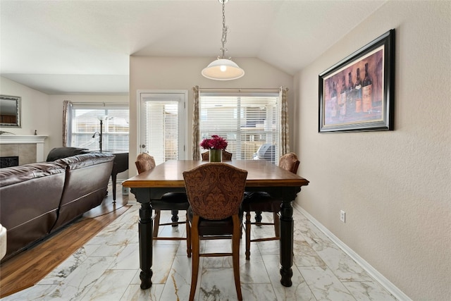 dining area with vaulted ceiling, light wood-type flooring, and a tile fireplace