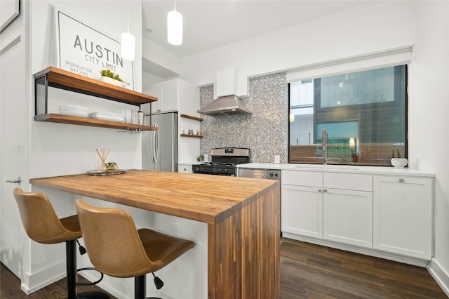 kitchen with stainless steel appliances, open shelves, butcher block counters, a sink, and wall chimney range hood