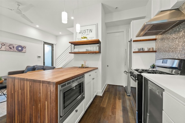 kitchen featuring wall chimney range hood, stainless steel appliances, pendant lighting, white cabinets, and dark wood-type flooring