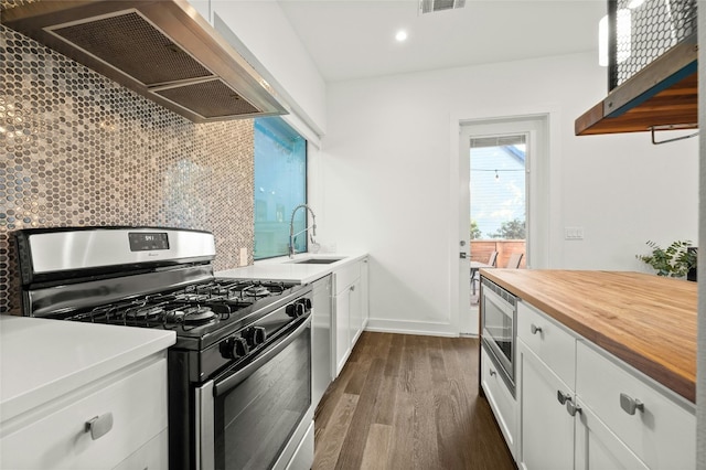 kitchen featuring stainless steel appliances, a sink, premium range hood, butcher block countertops, and backsplash