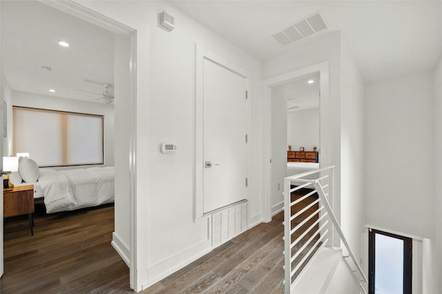 hallway with an upstairs landing, wood finished floors, and recessed lighting