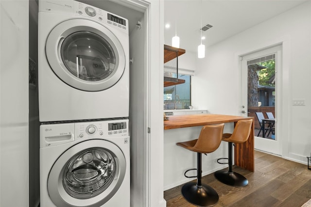 laundry area with stacked washer and clothes dryer, dark wood finished floors, and baseboards