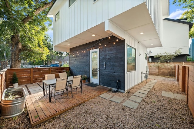 rear view of house featuring board and batten siding, a fenced backyard, a wooden deck, and outdoor dining space