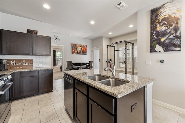 kitchen with an island with sink, stainless steel appliances, sink, light stone countertops, and tasteful backsplash