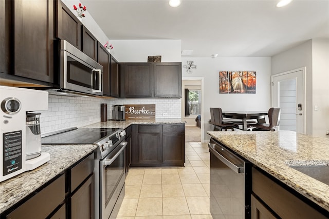 kitchen with tasteful backsplash, appliances with stainless steel finishes, light stone countertops, light tile patterned flooring, and dark brown cabinetry