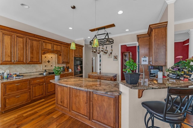 kitchen with kitchen peninsula, black double oven, decorative light fixtures, dark stone countertops, and dark hardwood / wood-style floors