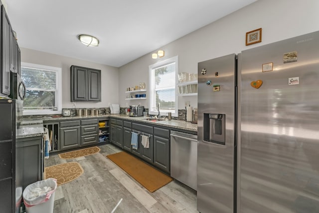 kitchen with gray cabinetry, sink, stone countertops, appliances with stainless steel finishes, and light wood-type flooring