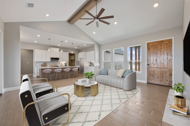 living room with sink, light wood-type flooring, ceiling fan, beamed ceiling, and high vaulted ceiling