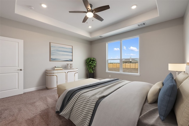 carpeted bedroom with ceiling fan and a raised ceiling