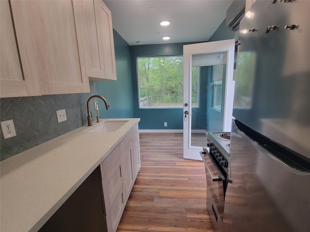 kitchen with light hardwood / wood-style flooring, a wall mounted air conditioner, backsplash, sink, and appliances with stainless steel finishes