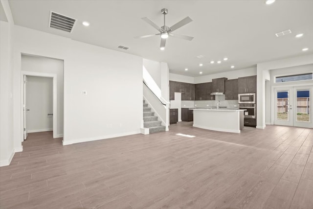 unfurnished living room featuring sink, french doors, light wood-type flooring, and ceiling fan