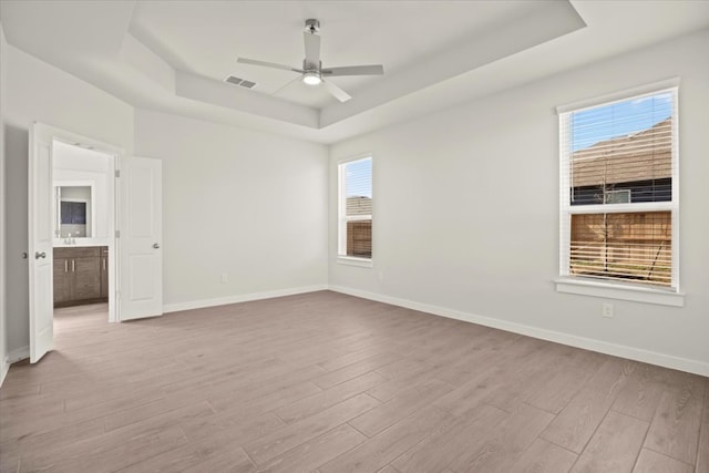 empty room featuring a tray ceiling, light hardwood / wood-style floors, and ceiling fan