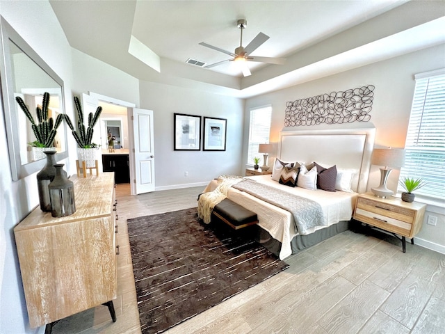 bedroom with ceiling fan, a raised ceiling, multiple windows, and hardwood / wood-style floors