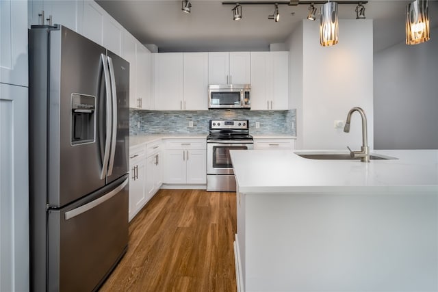 kitchen featuring appliances with stainless steel finishes, sink, pendant lighting, white cabinets, and hardwood / wood-style flooring