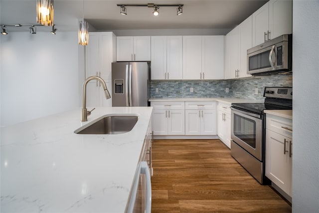 kitchen with sink, hanging light fixtures, stainless steel appliances, light stone countertops, and white cabinets