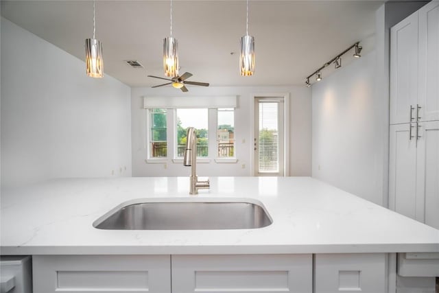 kitchen featuring visible vents, a ceiling fan, a sink, decorative light fixtures, and light stone countertops