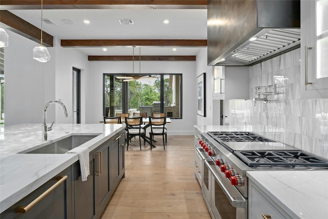 kitchen with light stone counters, beamed ceiling, appliances with stainless steel finishes, and light wood-type flooring