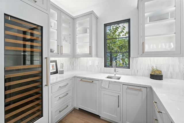 kitchen featuring hardwood / wood-style floors, beverage cooler, backsplash, sink, and light stone counters