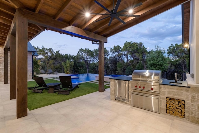 patio terrace at dusk featuring area for grilling, ceiling fan, sink, and exterior kitchen