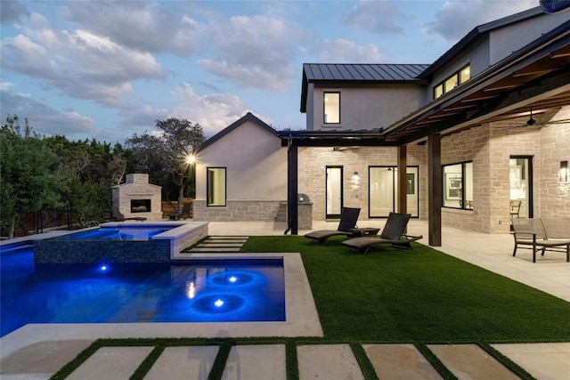 pool at dusk with an in ground hot tub, a yard, a patio area, and an outdoor stone fireplace