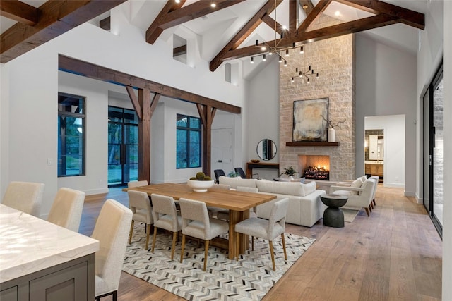 dining area with beam ceiling, light hardwood / wood-style floors, a stone fireplace, and high vaulted ceiling