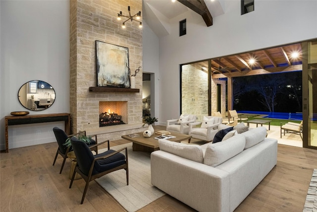 living room featuring hardwood / wood-style floors, beam ceiling, high vaulted ceiling, a chandelier, and a stone fireplace