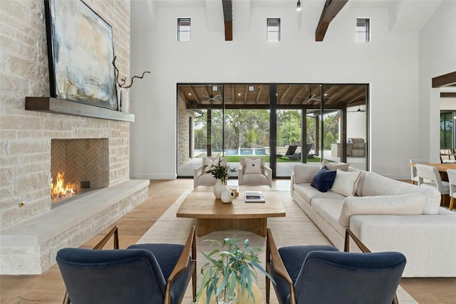 living room with light hardwood / wood-style flooring, a high ceiling, beam ceiling, and a fireplace