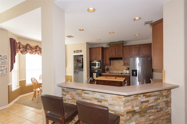 kitchen featuring kitchen peninsula, decorative backsplash, light tile patterned floors, black appliances, and sink