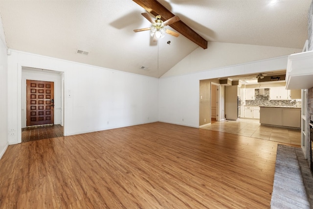 unfurnished living room with a textured ceiling, beamed ceiling, light wood-type flooring, and ceiling fan