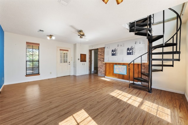 unfurnished living room featuring wood walls, a textured ceiling, wood-type flooring, and ceiling fan