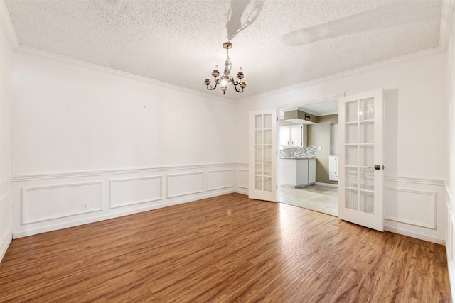 spare room featuring a chandelier, french doors, hardwood / wood-style flooring, and a textured ceiling