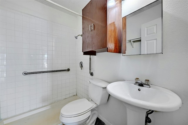 bathroom featuring a tile shower, toilet, and sink