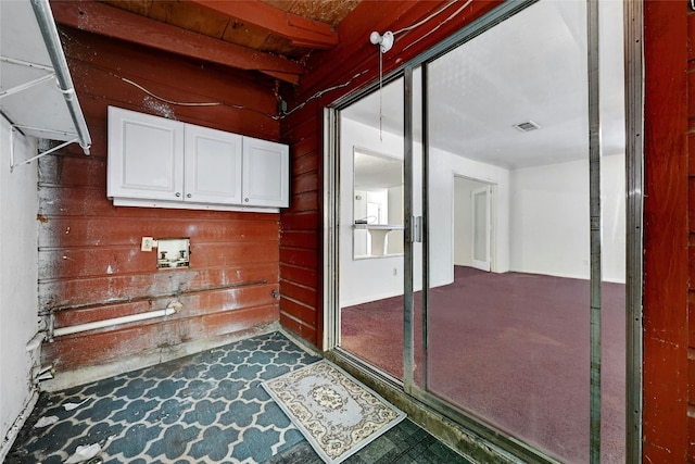 interior space featuring dark carpet, hookup for a washing machine, cabinets, and wood walls