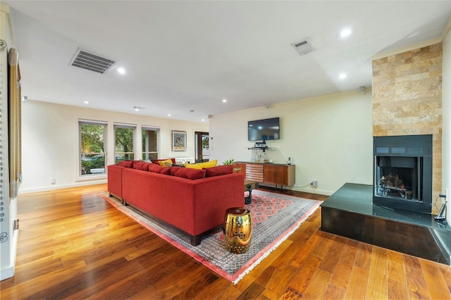 living room with crown molding, a fireplace, and wood-type flooring